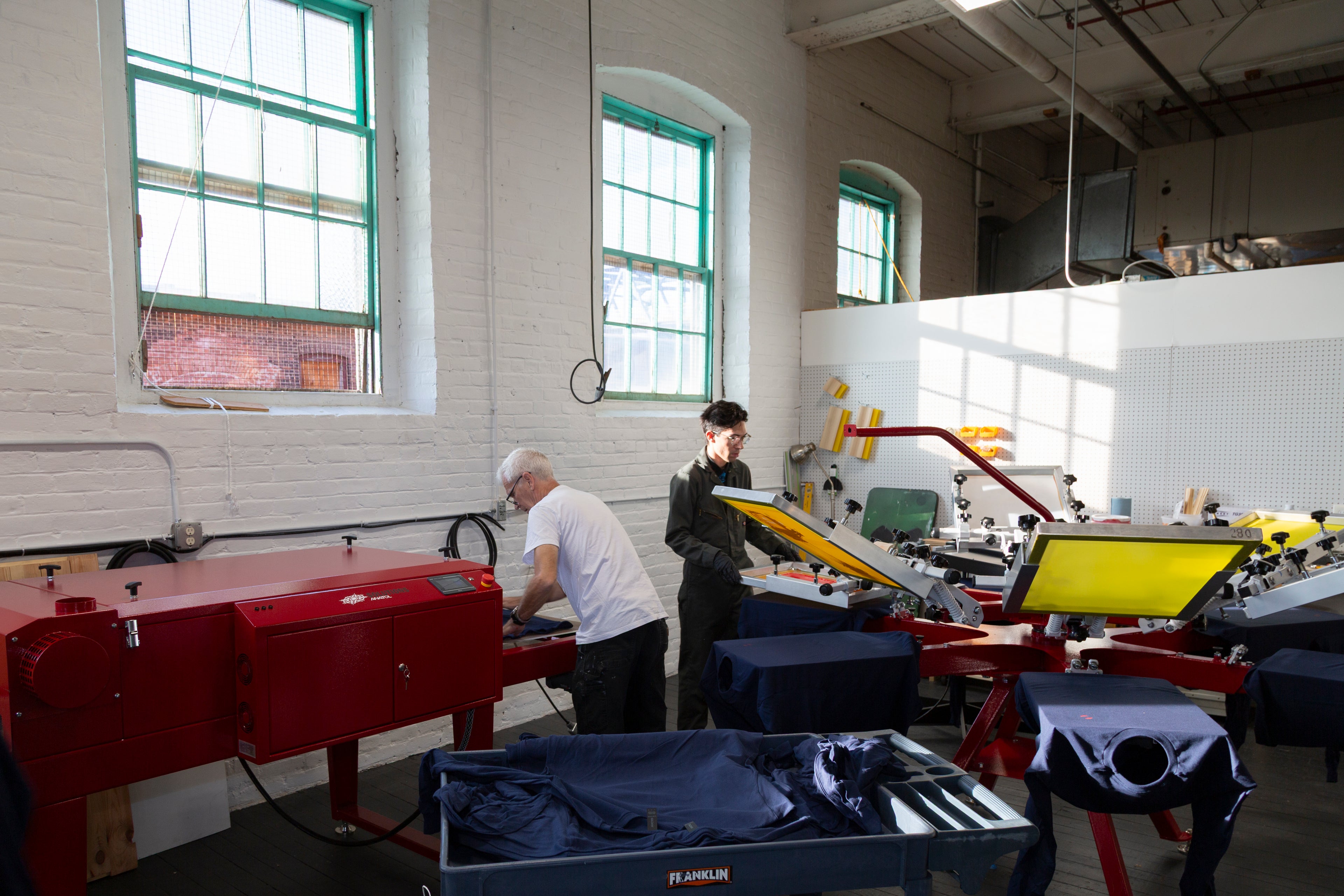 Two Frontside Factory craftsmen printing custom tee shirts in a Fall River MA Mill building
